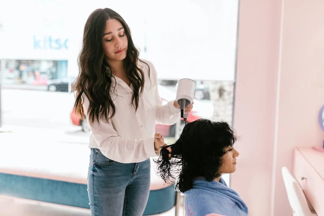 Donna con phon in mano che asciuga i capelli ad un altra donna